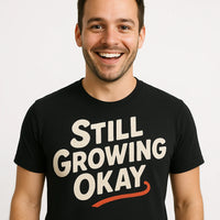 A person with short dark hair and a beard is smiling, wearing a black T-shirt with the text 