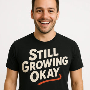 Close-up of the "Still Growing Okay" cream print on a premium Bella+Canvas black growth mindset t shirt