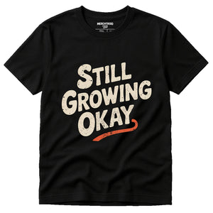 Black Growth Mindset T Shirt - "Still Growing Okay" graphic tee with cream print, flat lay product photo