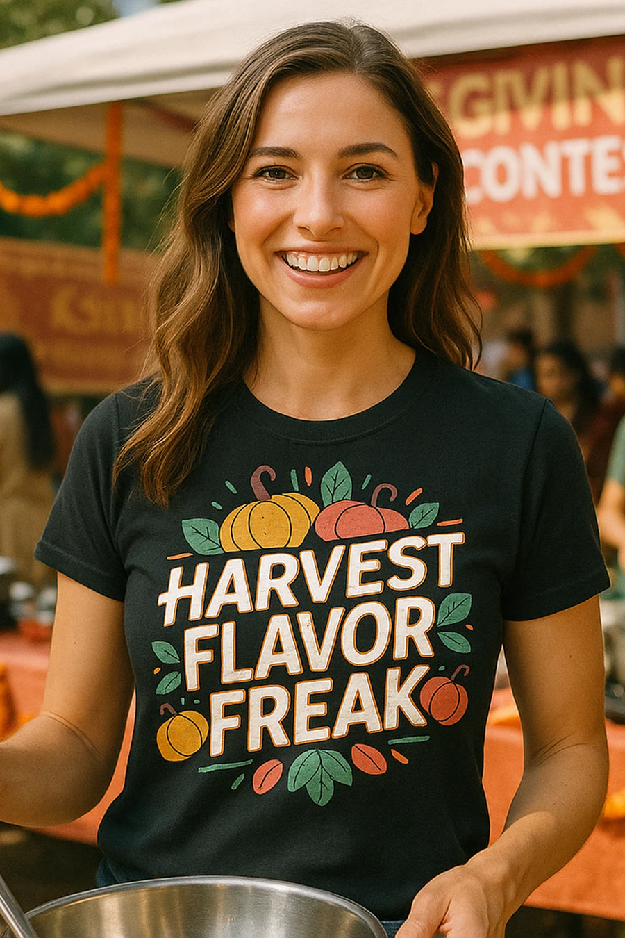 A person with long brown hair, smiling, wearing a black t-shirt with colorful graphics and text. They are holding a mixing bowl, standing outdoors at an event with decorations and people in the background.