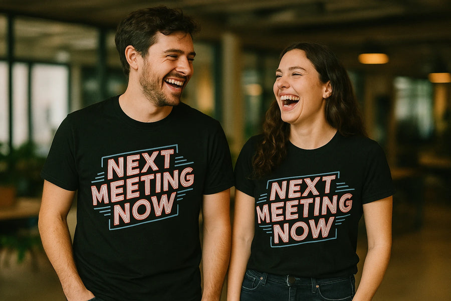 Two people are standing side by side, smiling and laughing. Both are wearing matching black T-shirts with the text "NEXT MEETING NOW" in bold, colorful letters. They appear to be in a casual indoor setting, possibly an office or coworking space.