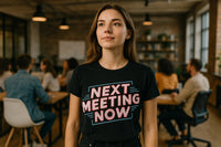 A person with long hair is standing in an office setting, wearing a black t-shirt that reads 