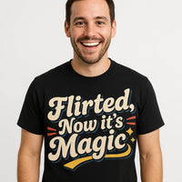 A person with short hair and facial hair is smiling while wearing a black T-shirt with bold, playful text on it. The shirt's design includes decorative elements like stars and swooshes in beige and colorful highlights. The background is plain white.
