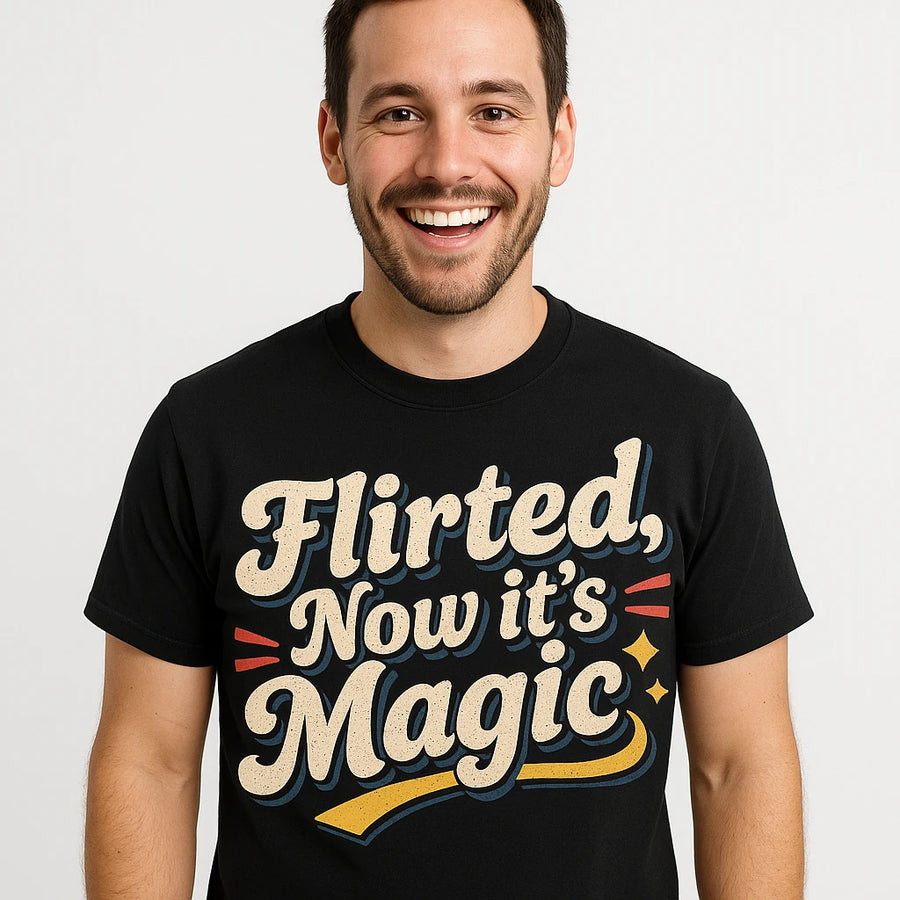 A person with short hair and facial hair is smiling while wearing a black T-shirt with bold, playful text on it. The shirt's design includes decorative elements like stars and swooshes in beige and colorful highlights. The background is plain white.